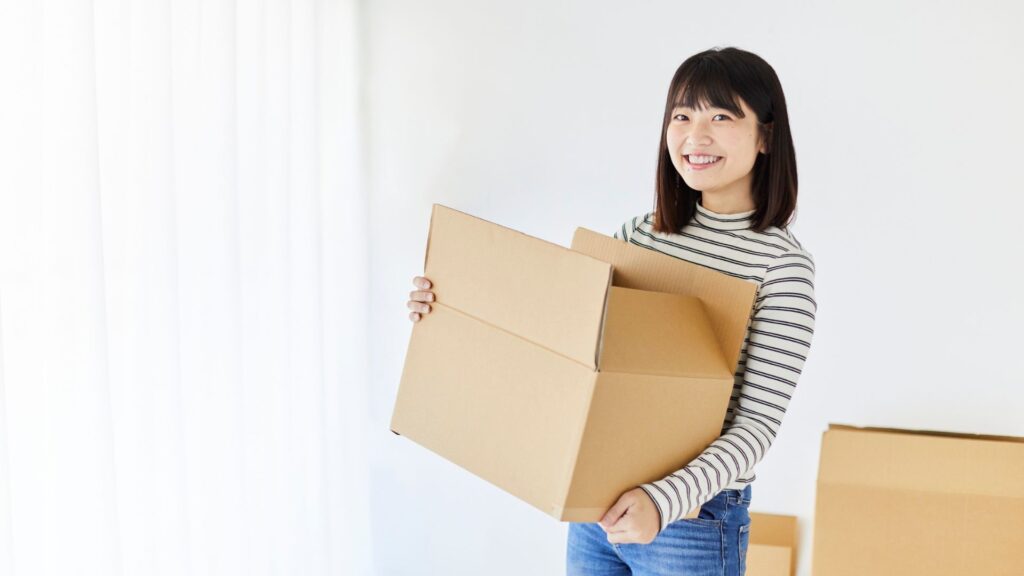 Smiling young woman holding an open cardboard moving box